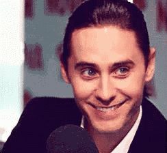 a man in a suit and tie is smiling and talking into a microphone .