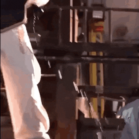 a man in a white shirt is standing in a dark room with a ladder in the background .
