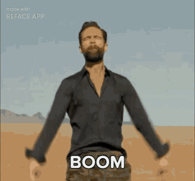 a man with a beard is standing in the middle of a desert with his arms outstretched and says boom .