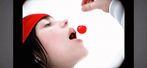 a woman in a red hat is biting a red cherry