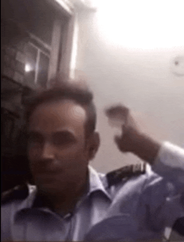 a man in a blue shirt is sitting in a room with his hand on his head