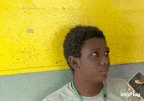 a young man is sitting in front of a yellow wall and holding a cell phone .
