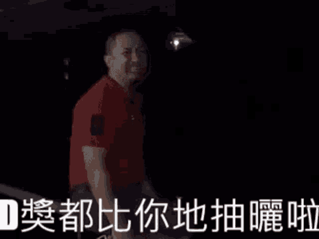 a man in a red shirt is dancing in the dark with chinese writing behind him