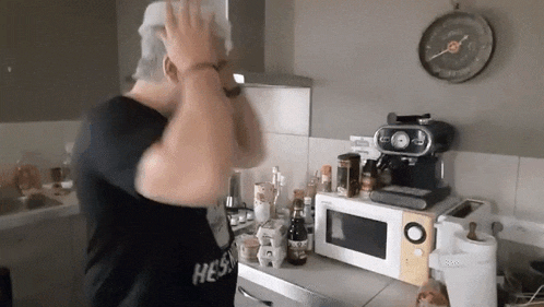 a man in a black shirt is standing in a kitchen with a microwave .