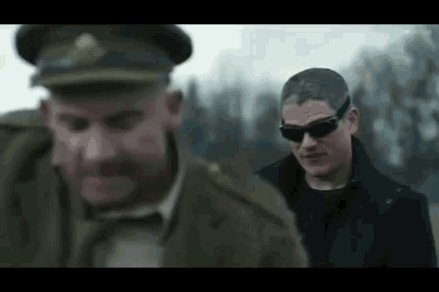 a man in a military uniform and sunglasses is standing next to another man .