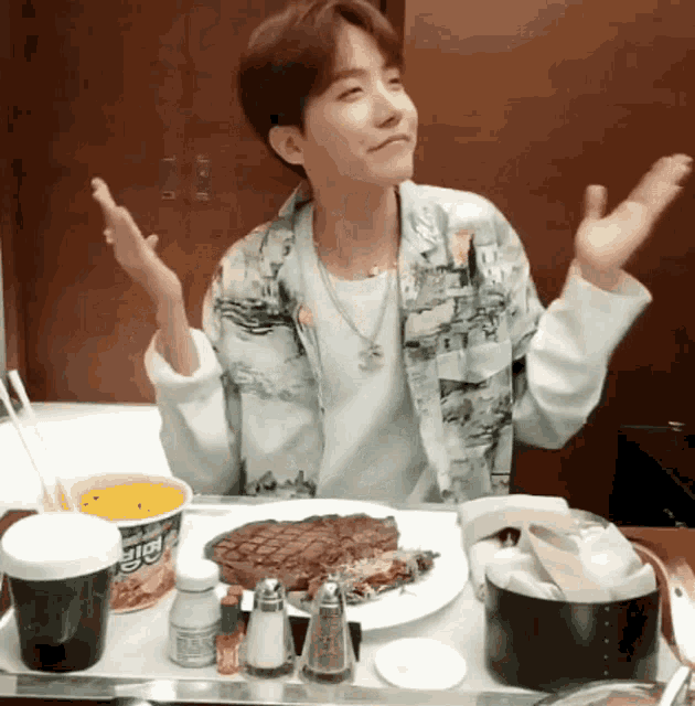 a man is sitting at a table with a plate of food and a cup of noodles that says ' beef '