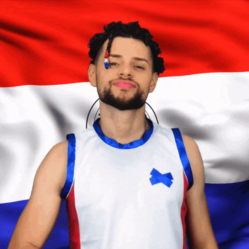 a man wearing a basketball jersey with a blue x on it stands in front of a red white and blue flag