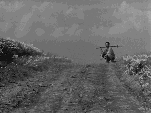 a black and white photo of a man kneeling down with a stick on his back