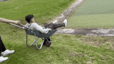 a man is laying in a wheelbarrow being pushed by another person .