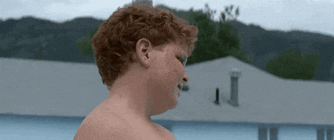 a shirtless man with red hair is standing in front of a building .