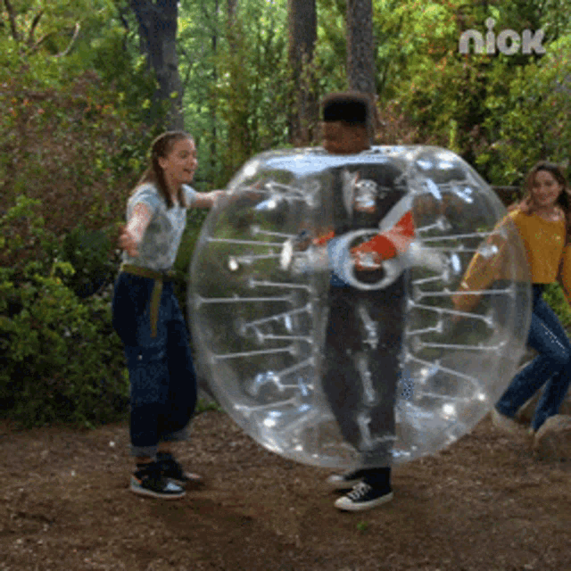 a group of kids are playing in a clear bubble with nick in the background