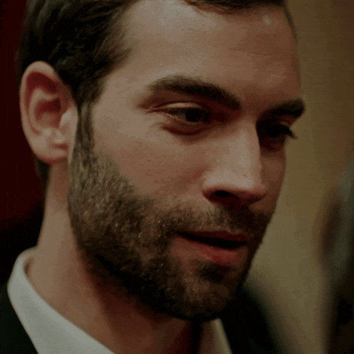 a close up of a man 's face with a beard and a white shirt