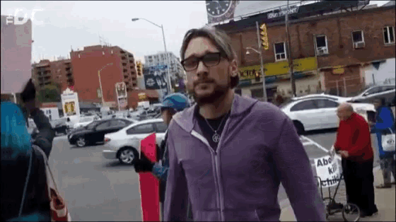 a man in a purple jacket is walking down a street with a sign that says abc