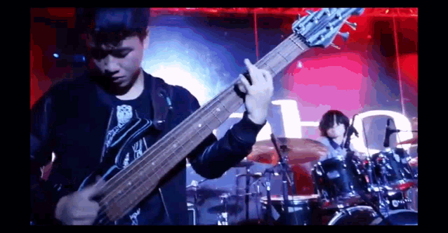 a man is playing a guitar in front of a drum set with the letter t on it