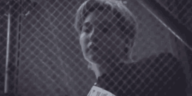 a man is behind a chain link fence holding a piece of paper in his hand .