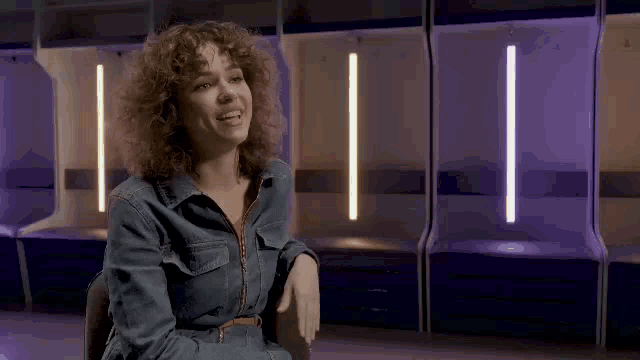 a woman with curly hair is sitting in a chair with her arms outstretched .