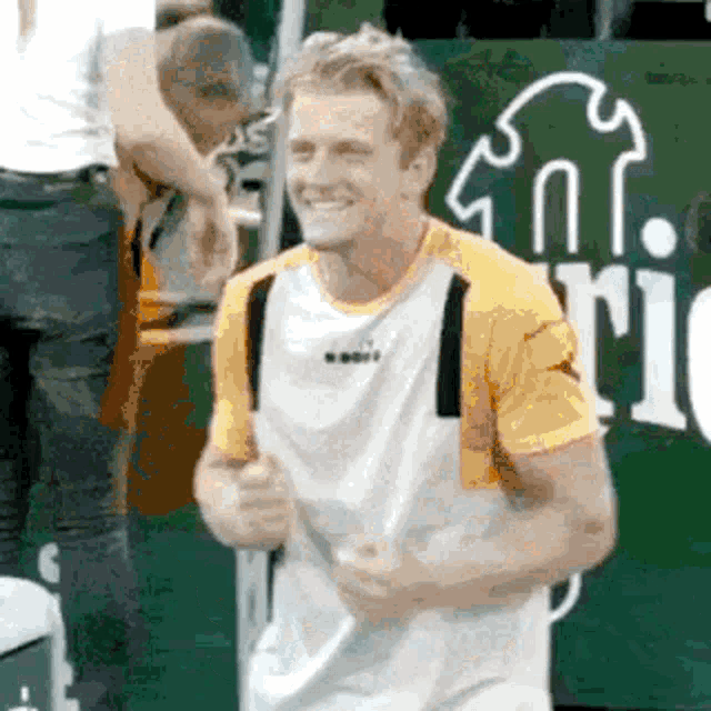 a man in a yellow and white shirt is smiling while holding a tennis racket .