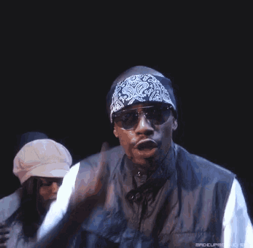 a man wearing sunglasses and a bandana pointing at the camera