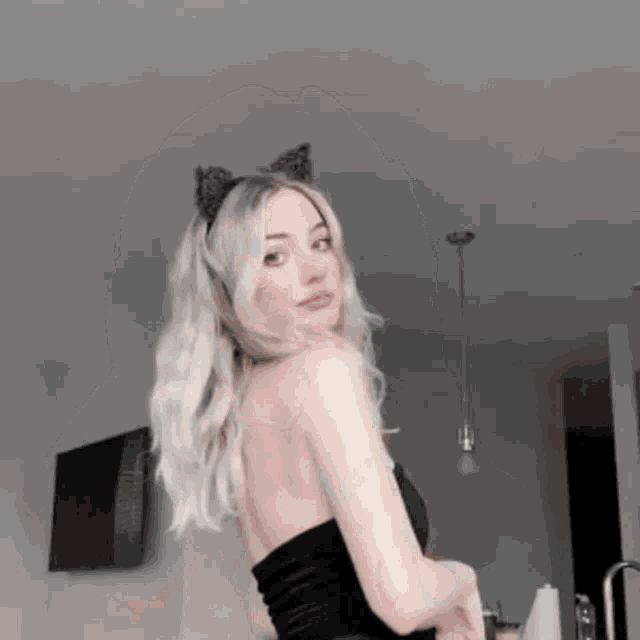 a woman wearing cat ears and a black top is standing in a kitchen .