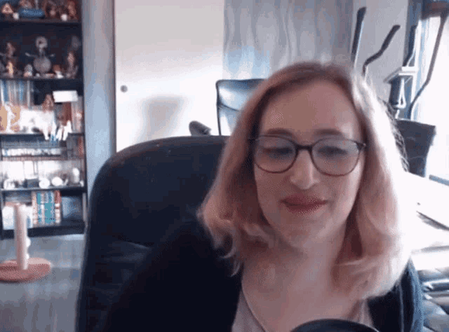 a woman wearing glasses is sitting in a chair in front of a bookshelf