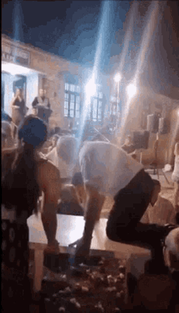 a man is kneeling down in front of a table with a woman standing behind him .