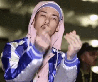 a man wearing a hooded jacket and a pink headband is making a heart shape with his hands .