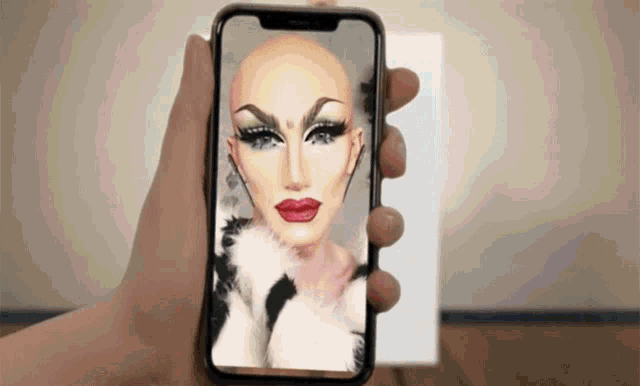 a person is holding a phone with a drag queen on the screen
