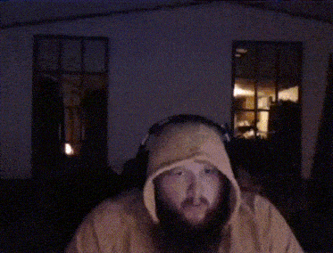a man with a beard is dancing with his arms in the air in a dark room