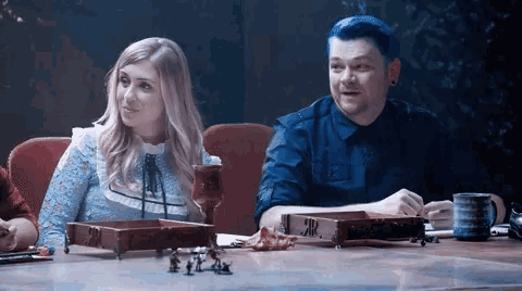 a man and a woman are sitting at a table with miniature figures