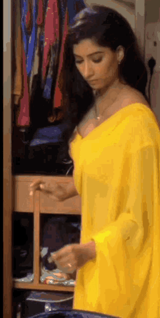 a woman in a yellow saree is standing in a closet looking at clothes .