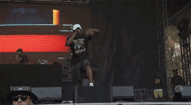a man stands on a stage with a denzel curry sign behind him