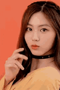 a woman wearing a choker and a yellow shirt is looking at the camera .