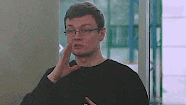 a man wearing glasses and a black sweater is making a funny face