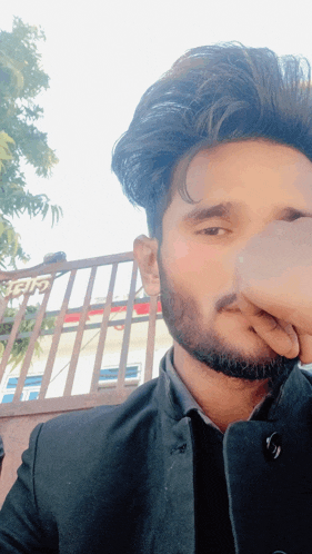 a man with a beard is covering his nose in front of a fence that says ' shree ' on it