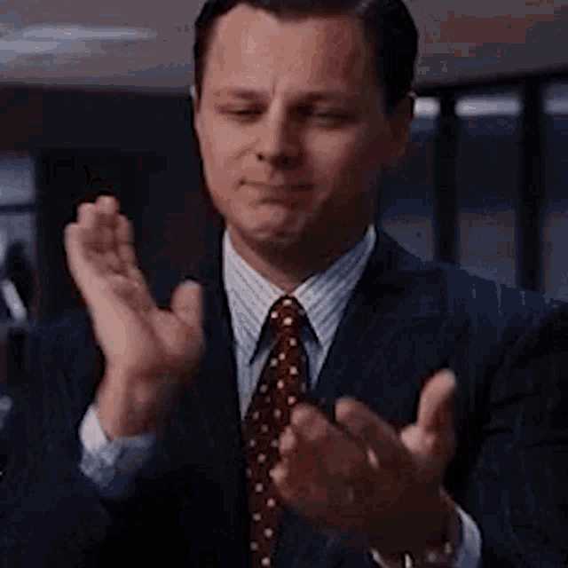 the man is wearing a suit and tie and clapping his hands .