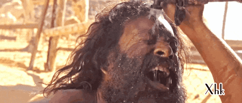 a man with a beard is drinking water from a bottle with xhk written on the bottom right