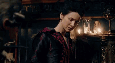 a woman in a red and black dress is standing next to a man in a room with candles .