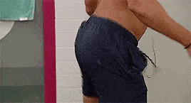 a shirtless man in blue swim trunks is standing in a shower .