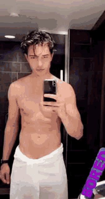 a shirtless man with a towel around his waist is taking a selfie in a bathroom mirror .