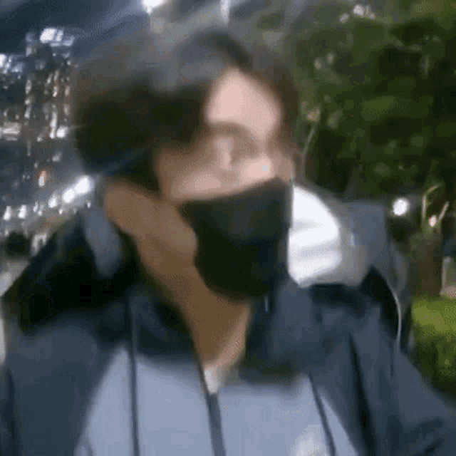 a man wearing a mask and glasses is standing in front of a tree .