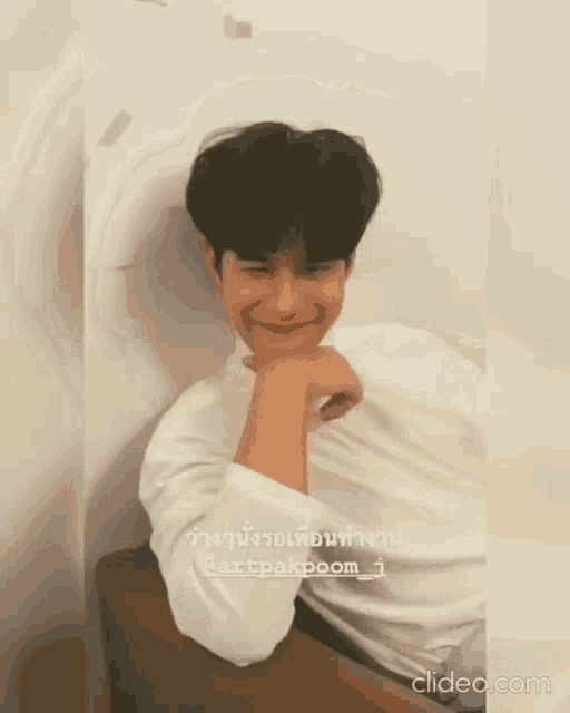a man in a white shirt is sitting down with his hand on his chin and smiling .