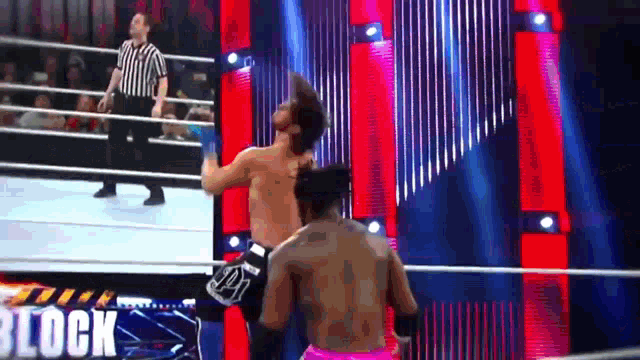two men are wrestling in a wrestling ring with a referee standing behind them