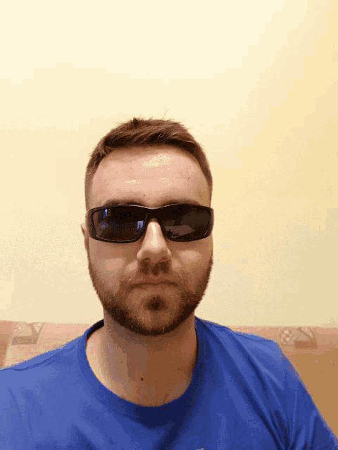 a man wearing sunglasses and a blue shirt has a beard