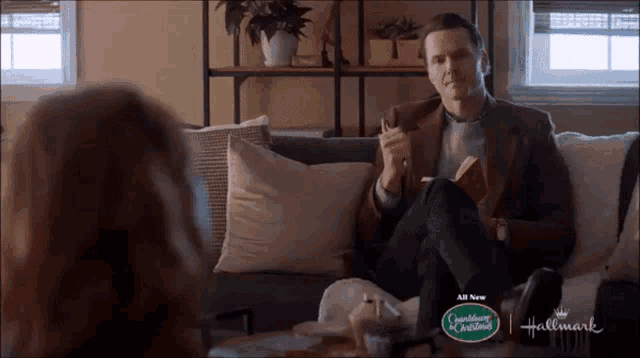 a man is reading a book while sitting on a couch with a hallmark logo on it