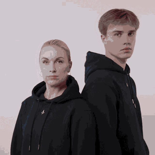 a man and a woman standing back to back wearing black sweatshirts