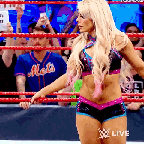 a woman is standing in a wrestling ring wearing a mets jersey