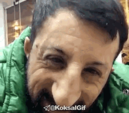 a man with a beard wearing a green jacket is making a face .