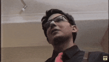 a man wearing glasses and a red tie is looking up at something