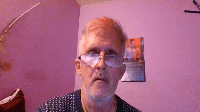 a man wearing glasses stands in front of a pink wall