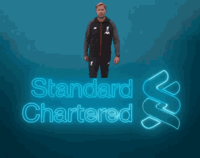 a man standing in front of a neon sign that says standard chartered